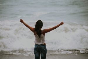 woman with arms open wide facing the ocean